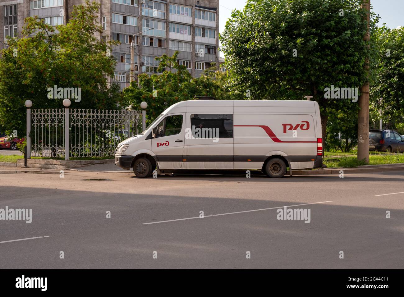 An einem sonnigen Sommertag steht ein Minibus mit dem Logo der russischen Eisenbahngesellschaft auf der Straßenseite in der Nähe eines Metallzauns. Stockfoto