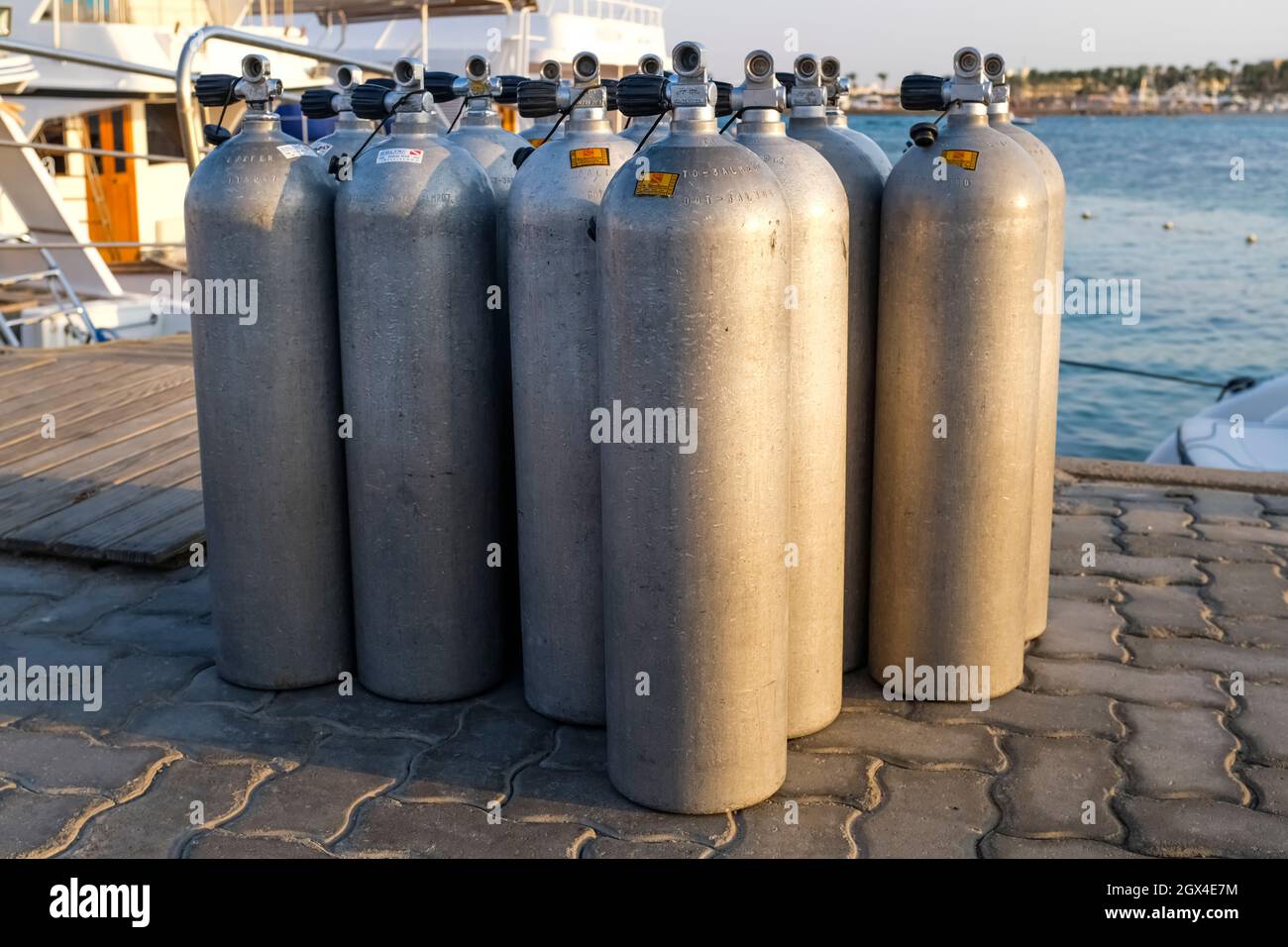 Viele Alu-Tauchsauerstofftanks stehen vor den grünen Strandbüschen und Felsen auf dem Sand in Thailand mit Kopierraum Stockfoto