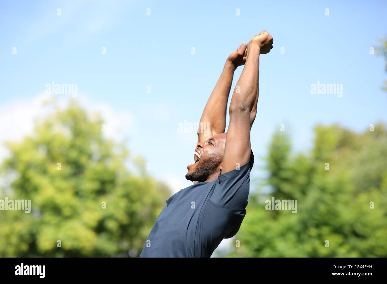 Seitenansicht Porträt eines aufgeregten schwarzen Mannes, der in einem Park die Arme hebt Stockfoto