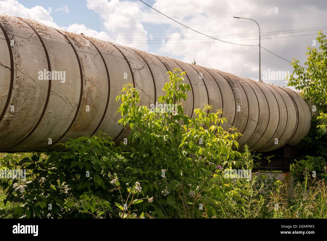 Ein Teil der Pipeline der Oberflächenwärmeleitung des städtischen Hauptwärmenetzes auf einer Stahlbetonstütze unter dem Gras an einem sonnigen Sommer d Stockfoto