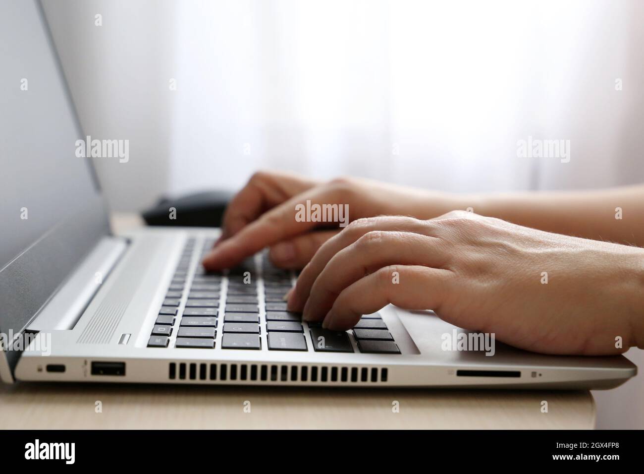 Weibliche Hände auf Laptop-Tastatur auf einem Schreibtisch in Sonnenlicht. Frau Typen auf der Laptop-Tastatur sitzen in der Nähe des Fensters, Remote-Arbeit Stockfoto