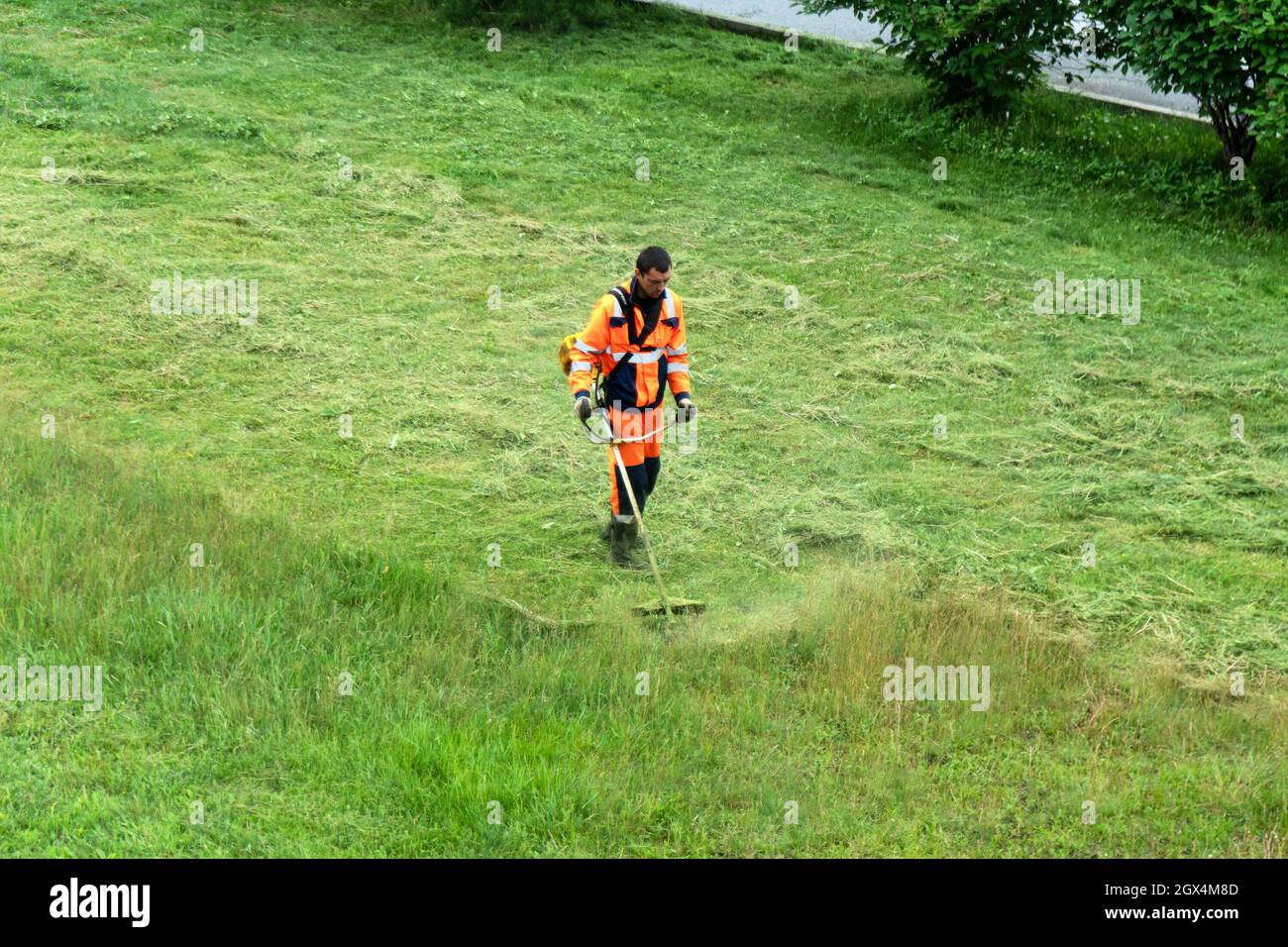 Ein Arbeiter in orangefarbenen Overalls mäht an einem bewölkten Sommertag den Rasen. Stockfoto