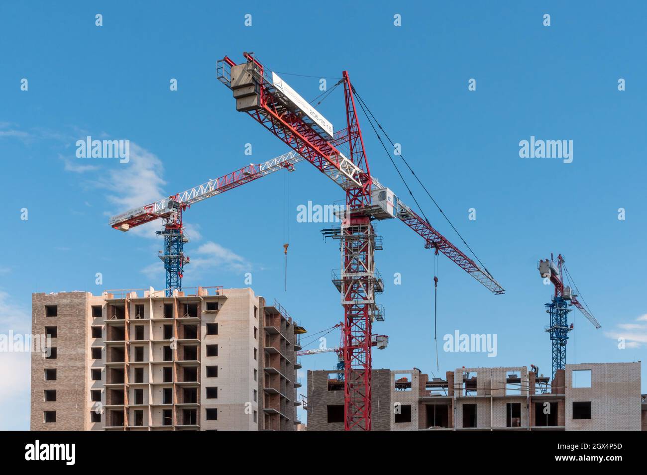 Turmdrehkrane arbeiten am Bau von gemauerten Wohngebäuden vor dem Hintergrund eines blauen Himmels. Stockfoto