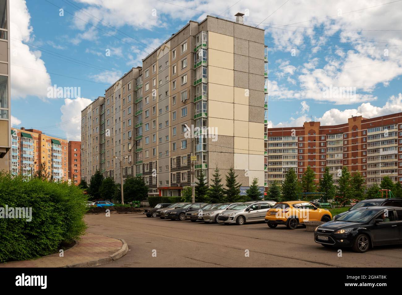 Zwischen den neuen Hochhäusern steht ein zehnstöckiges Wohnhaus, das während der Breschnew-Ära erbaut wurde, Autos werden im Sommer in der Nähe geparkt. Stockfoto