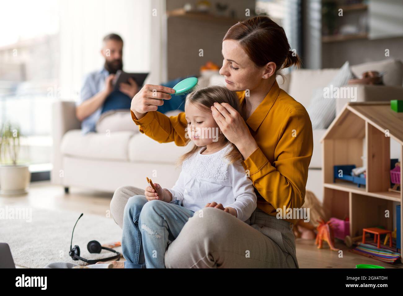 Mutter beushing ihrer kleinen Tochter zuhause, im Alltag und im Home Office mit Kinderkonzept Haare. Stockfoto