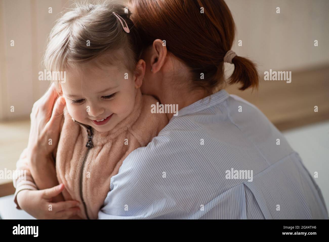 Mutter mit kleiner Tochter umarmt sich morgens in der Eingangshalle und geht zur Arbeit und zum Kindergarten. Stockfoto
