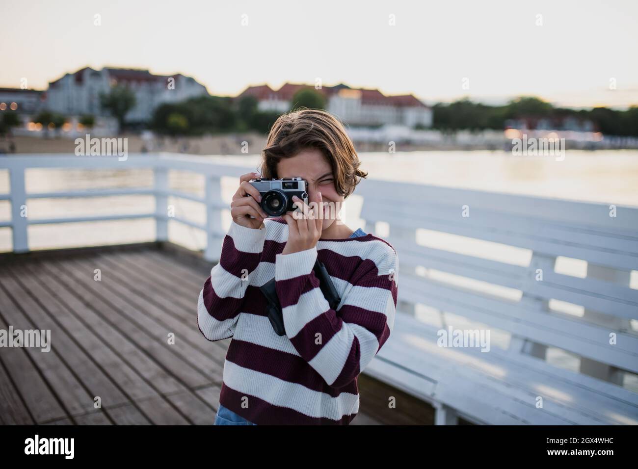 Präteen Mädchen Tourist fotografieren mit Kamera auf Pier am Meer bei Sonnenuntergang, Sommerurlaub Konzept. Stockfoto