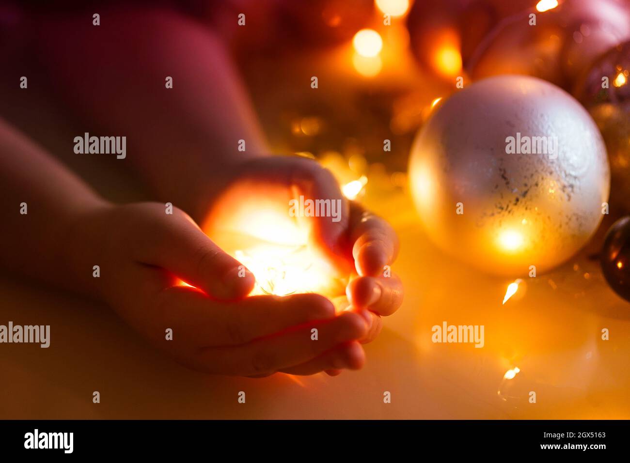 Weihnachten Gold glänzendes Licht in den Händen der Kinder. Weihnachtshintergrund mit weihnachtskugeln, Dekorationen und Lichtern. Neujahrskarte. Stockfoto