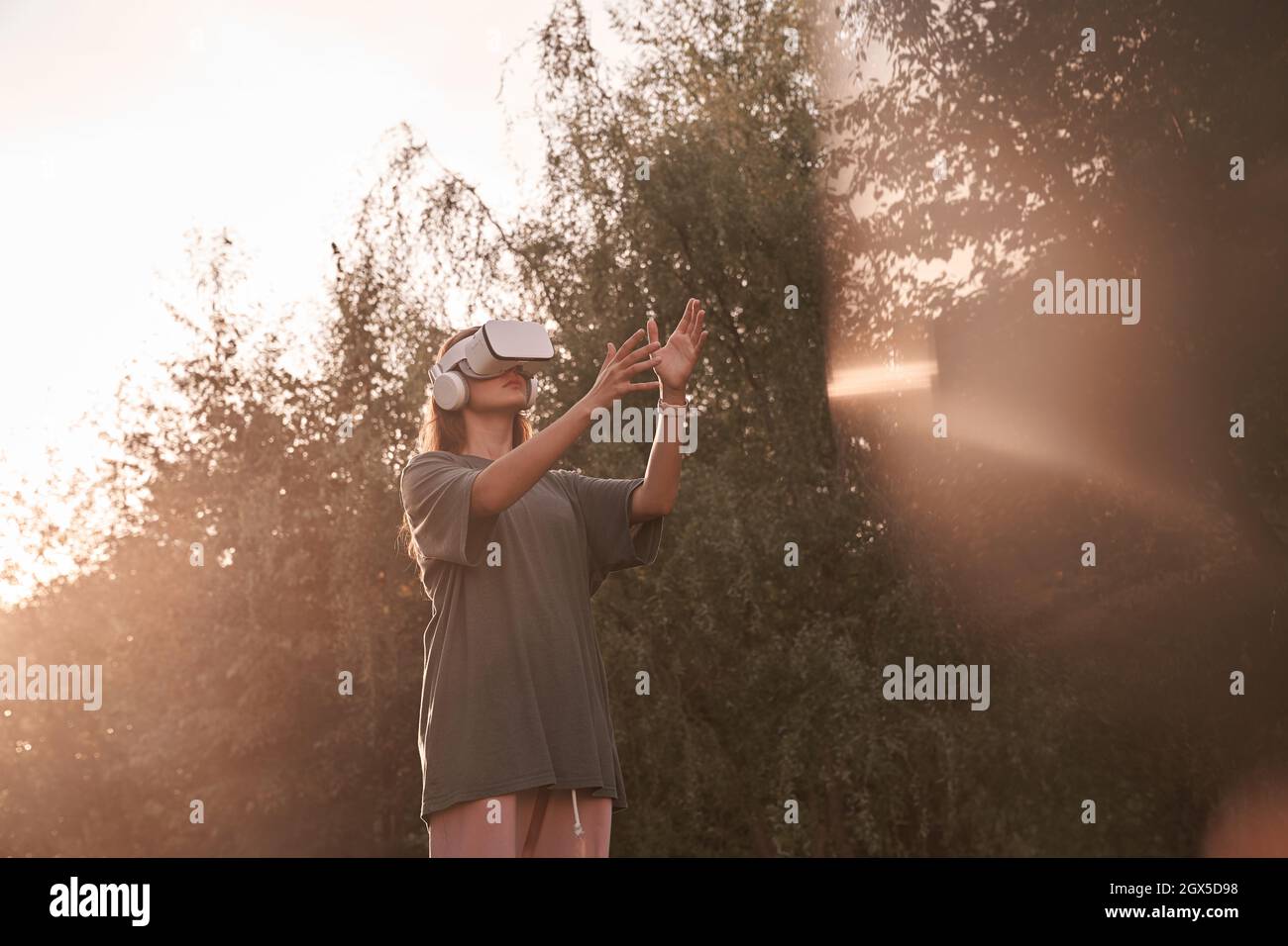 Ein Mädchen mit einer Virtual-Reality-Brille. Er reicht seine Hände an den Sonnenstrahl. Hochwertige Fotos Stockfoto