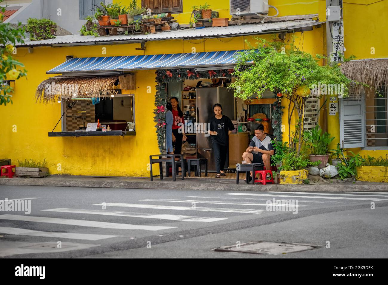 Vietnamesische Straße mit gelb gestrichenen Gebäuden, die mit Blumen geschmückt sind. Kleines Restaurant mit Tischen an der Straße. Nha Trang, Vietnam: 2020-10-23 Stockfoto