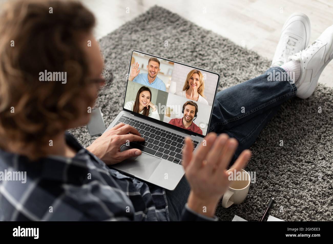 Millennial kaukasischen Kerl Freiberufler winkt Hand, haben Online-Treffen mit Mitarbeitern auf Laptop-Bildschirm Stockfoto