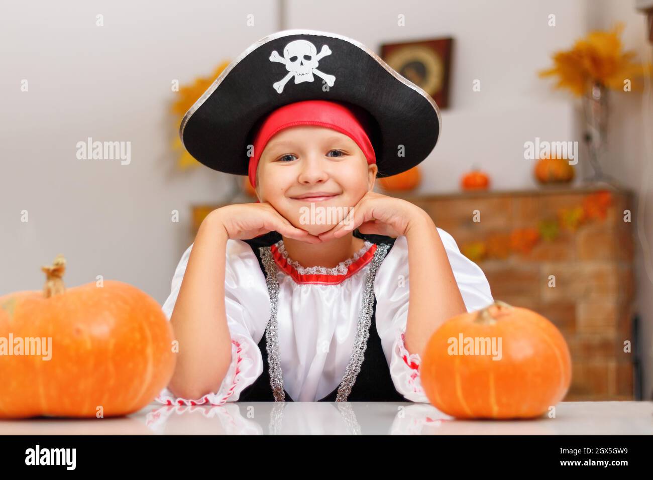 Halloween zu Hause feiern. Ein kleines Mädchen, das als Pirat gekleidet ist, sitzt mit Kürbissen an einem Tisch. Stockfoto