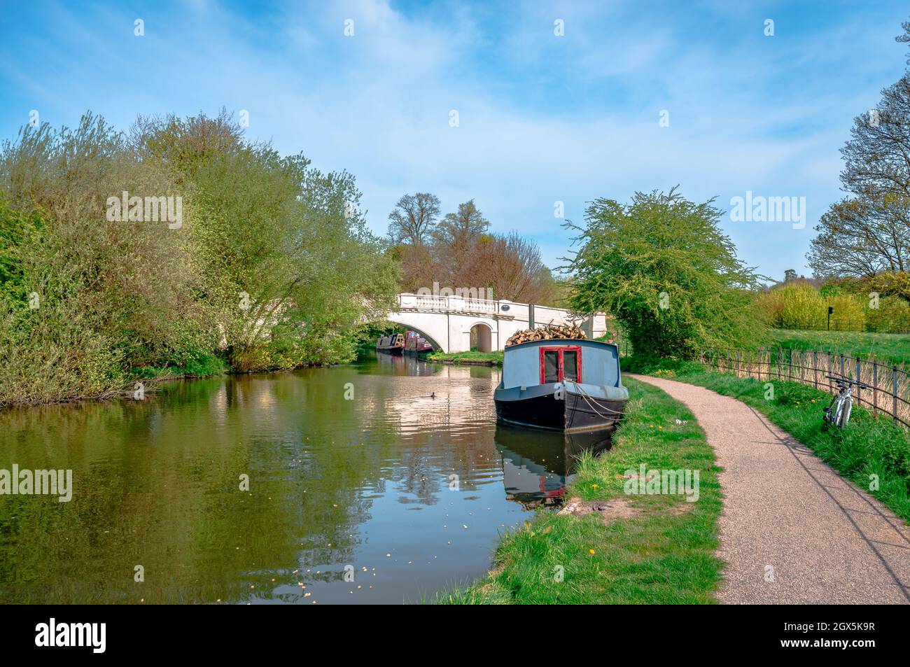 Blick auf den Fluss Gade (Grand Union Canal) und die Grove Bridge (Grove Ornamental Bridge No 164) im Cassiobury Park, England. Festgetäutes, schmale Boot. Stockfoto