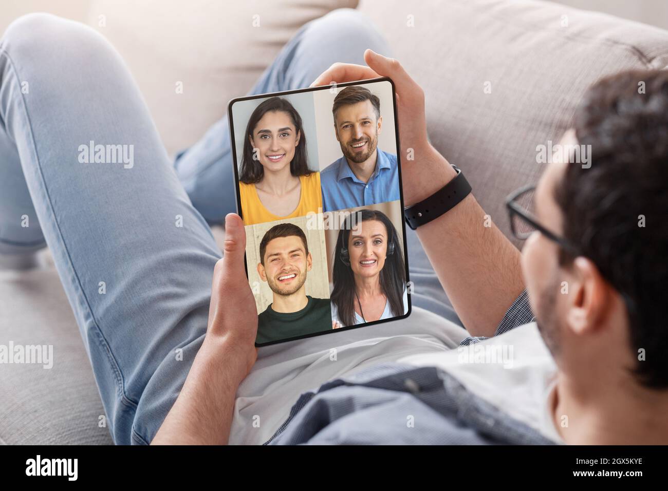 Europäischer Millennial Mann Rest auf dem Sofa Treffen Sie sich mit Freunden auf dem Tablet-Bildschirm Stockfoto