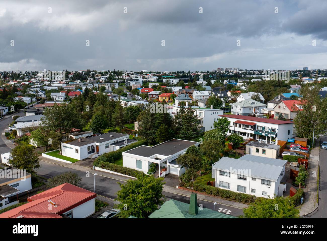 Luftaufnahme von modernen Cottages und üppigen Bäumen in der Nähe von Asphaltstraße gegen bewölkten grauen Himmel in der Stadt. Stockfoto