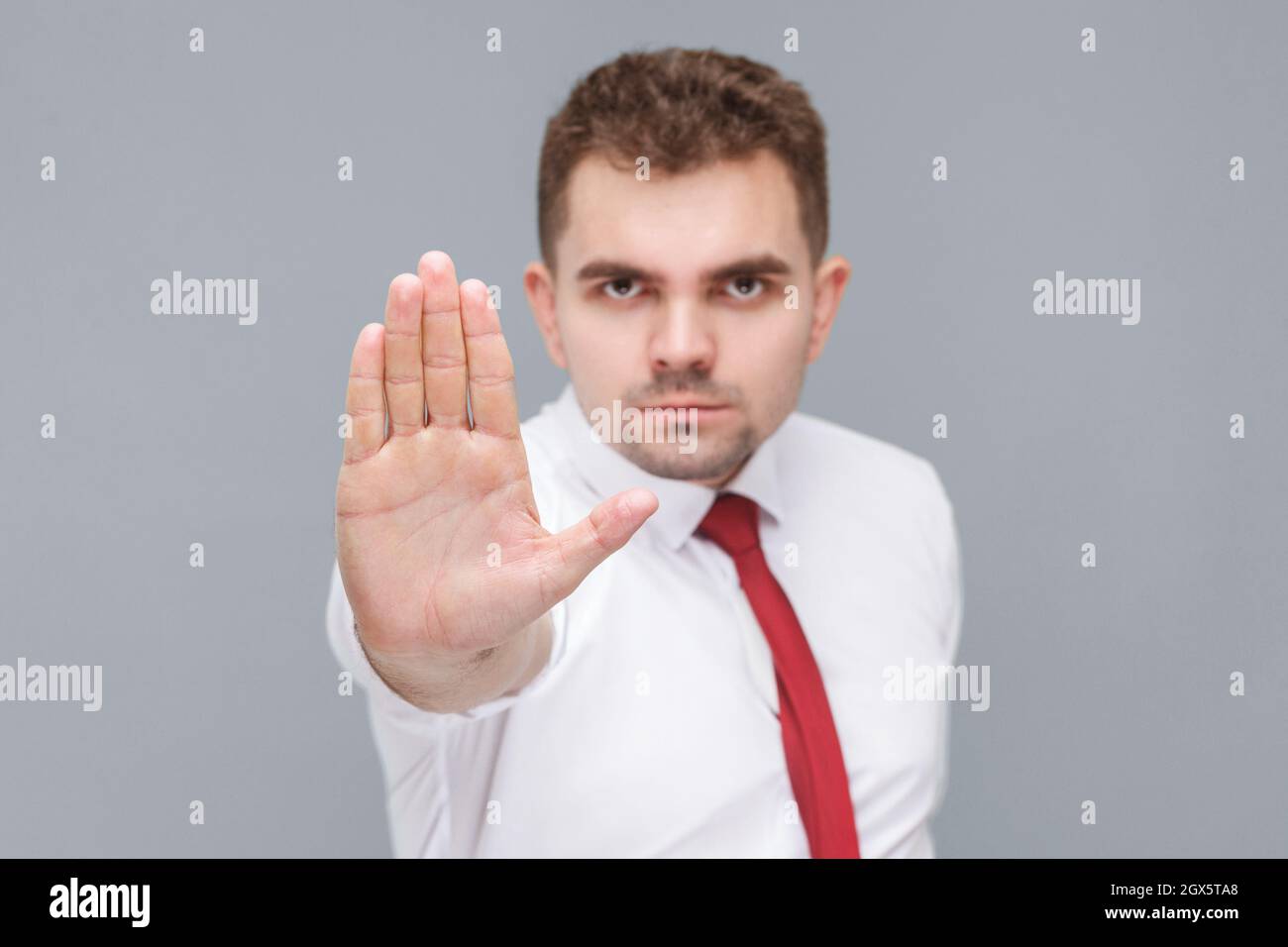 Hör auf. Porträt eines jungen hübschen ernsten Mannes in weißem Hemd und Krawatte stehen mit Stop-Hand und Blick auf die Kamera mit ernstem Gesicht. Indoor isoliert auf grauem Hintergrund. Stockfoto