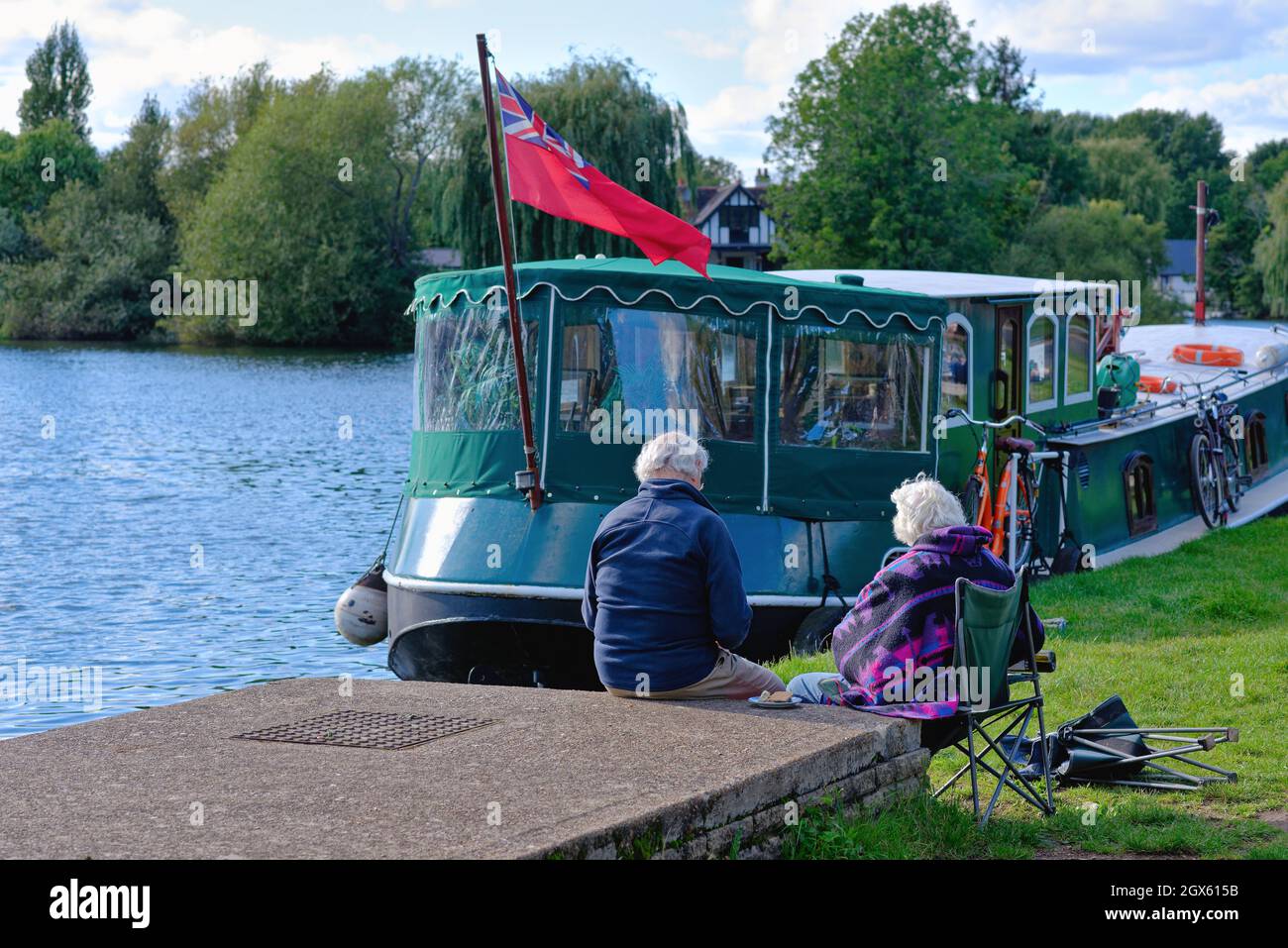 Ein älteres Paar, das am Flussufer in Shepperton sitzt und an einem Sommertag in Surrey England einen kleinen Snack genießt Stockfoto