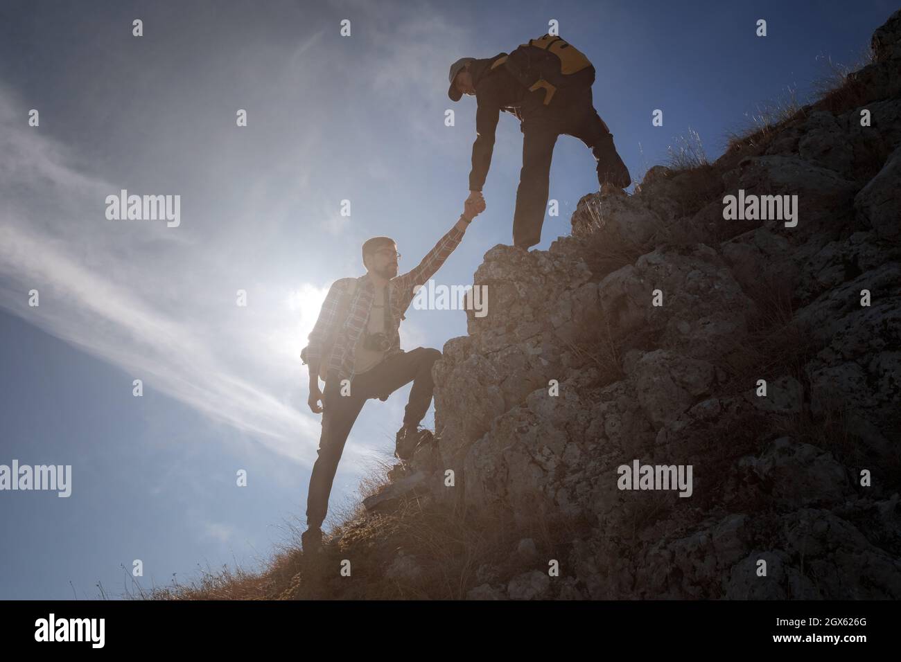 Hilfe- und Hilfekonzept. Silhouetten von zwei Menschen, die Berge besteigen und gegen den blauen Himmel helfen. Gehen Sie in den Wolken. Discovery Travel Direc Stockfoto
