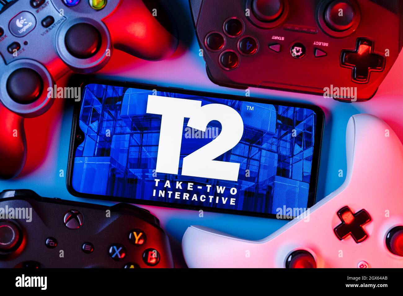 Ein Smartphone mit dem Take-Two-Logo auf dem Bildschirm, umgeben von Gamepads. Stockfoto