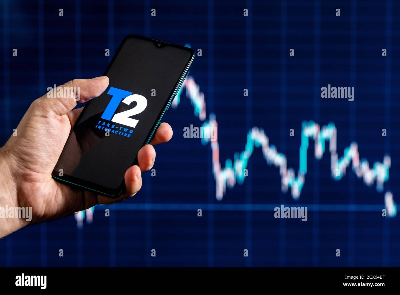 Ein Smartphone mit dem Take-Two-Logo in der Hand. Aktiendiagramm im Hintergrund. Stockfoto