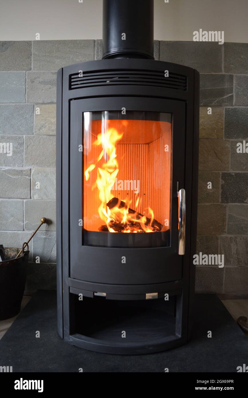 Feuer in neuem Holzofen auf Schieferboden mit Fliesen dahinter. Stockfoto