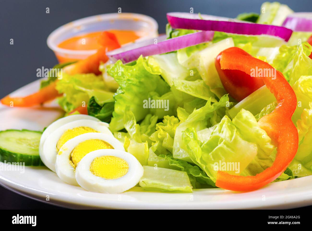 Salat mit einer Seite von vereierten Eiern. Auf einem Teller mit einer kleinen Tasse Dressing sitzen weiße und gelbe Eier. Daneben ist ein Salat gemacht Stockfoto