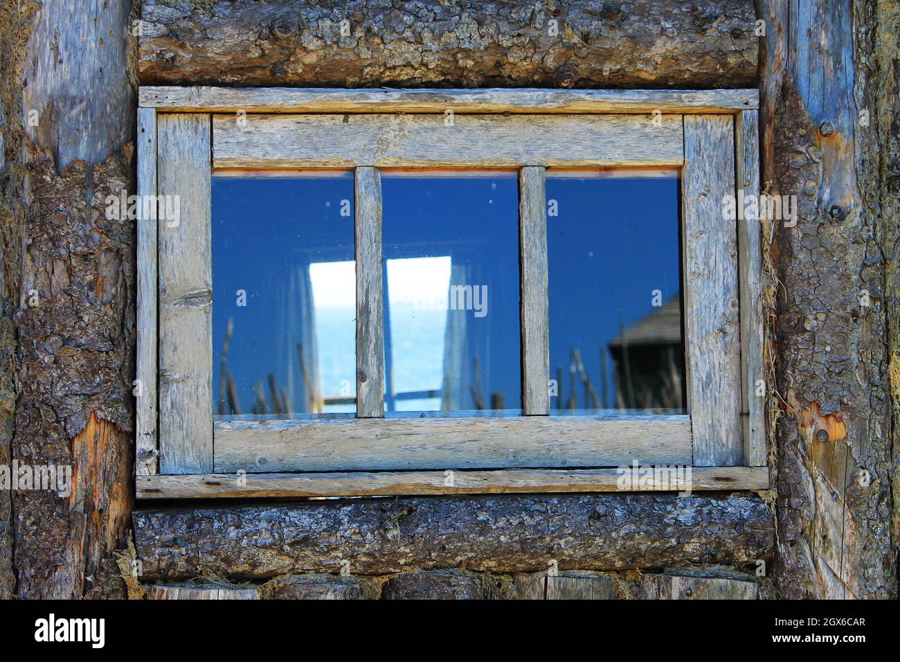 Durch ein altes, holzgerahmtes Fenster in der Wand einer Blockhütte und durch das Fenster an der gegenüberliegenden Wand auf den Atlantischen Ozean blicken. Stockfoto