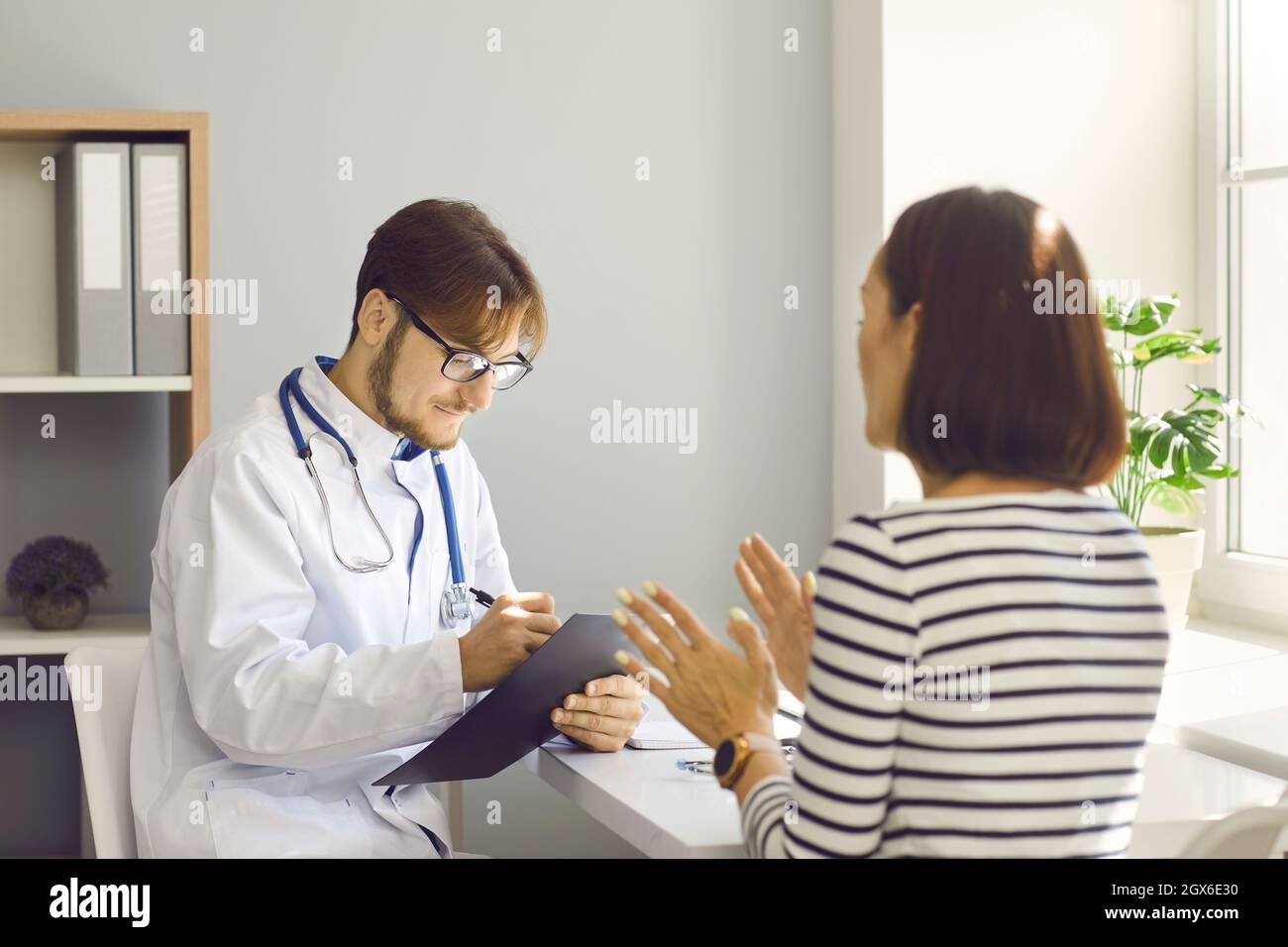 Männlicher Arzt schreibt bei der ärztlichen Untersuchung ein Rezept oder macht Notizen in der Patientenkarte. Stockfoto