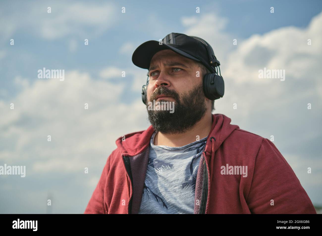 Ein Mann mittleren Alters in Kopfhörern im Freien, der vor dem Hintergrund des Himmels Musik hört Stockfoto