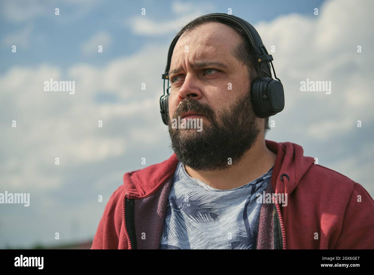 Ein Mann mittleren Alters in Kopfhörern im Freien, der vor dem Hintergrund des Himmels Musik hört Stockfoto