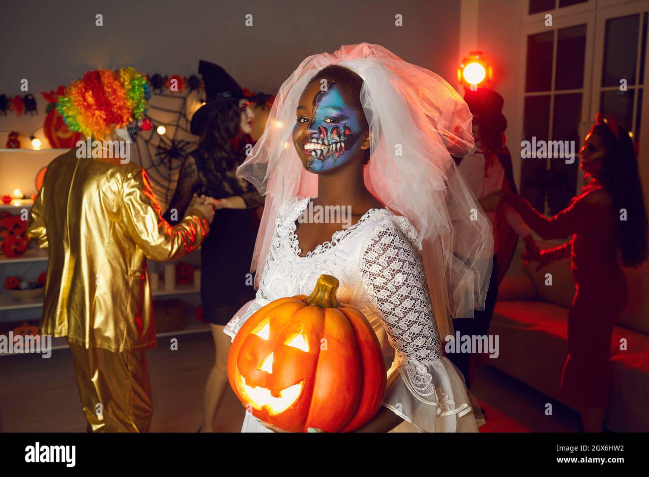 Porträt einer schwarzen Frau, die als Tote Braut gekleidet ist und Jack-o-Laterne auf der Halloween-Party hält Stockfoto