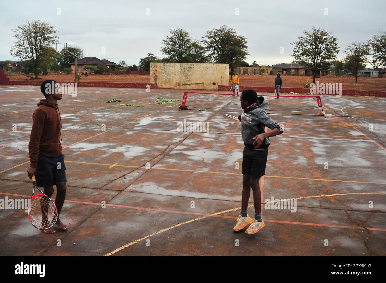 Junge Jungen spielen Tennis auf einem Feld im ländlichen Dorf Thomo in Limpopo, Südafrika. Sie spielen mit zerbrochenen Schlägern und barfuß auf einem alten Platz Stockfoto