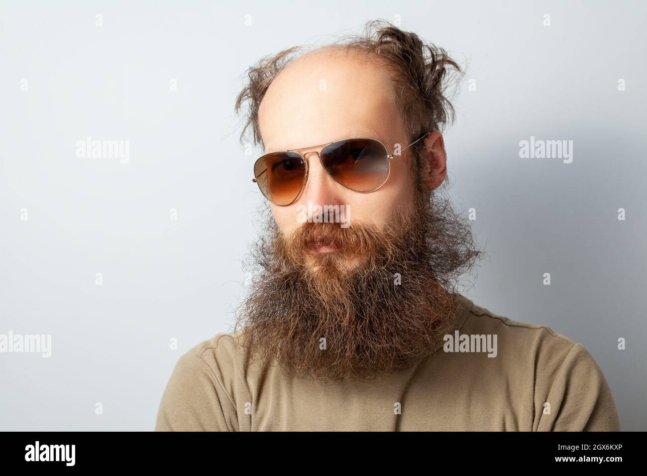 Porträt eines erwachsenen, gutaussehenden, ernsthaften Mannes, der mit ruhigem Gesichtsausdruck auf die Kamera schaut, eines kahlen bärtigen Mannes mit T-Shirt und Sonnenbrille. Innenaufnahme des Studios isoliert auf grauem Hintergrund. Stockfoto