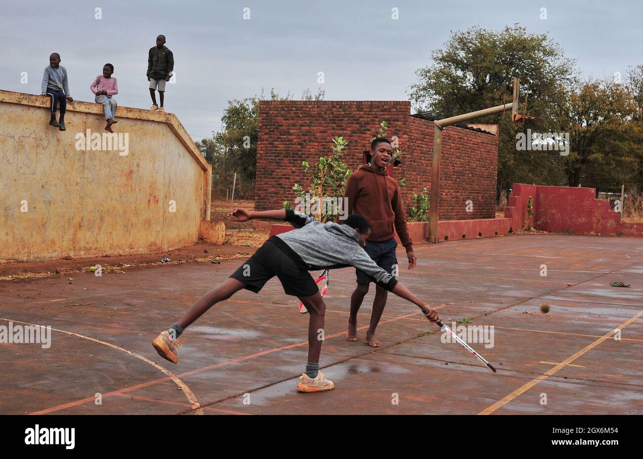 Junge Jungen spielen Tennis auf einem Feld im ländlichen Dorf Thomo in Limpopo, Südafrika. Sie spielen mit zerbrochenen Schlägern und barfuß auf einem alten Platz Stockfoto