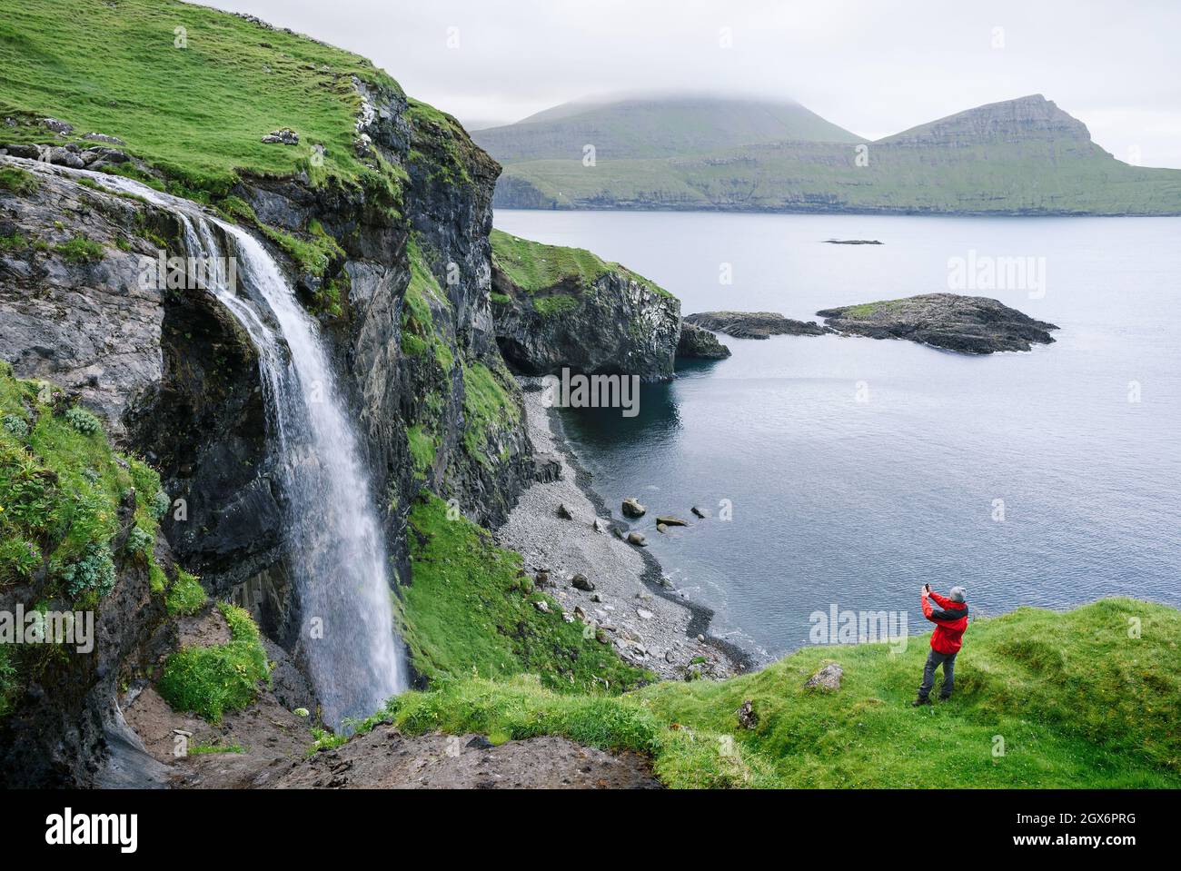 Ein Tourist fotografiert den Wasserfall Skardsafossur auf der Insel Vagar, Färöer-Inseln Stockfoto