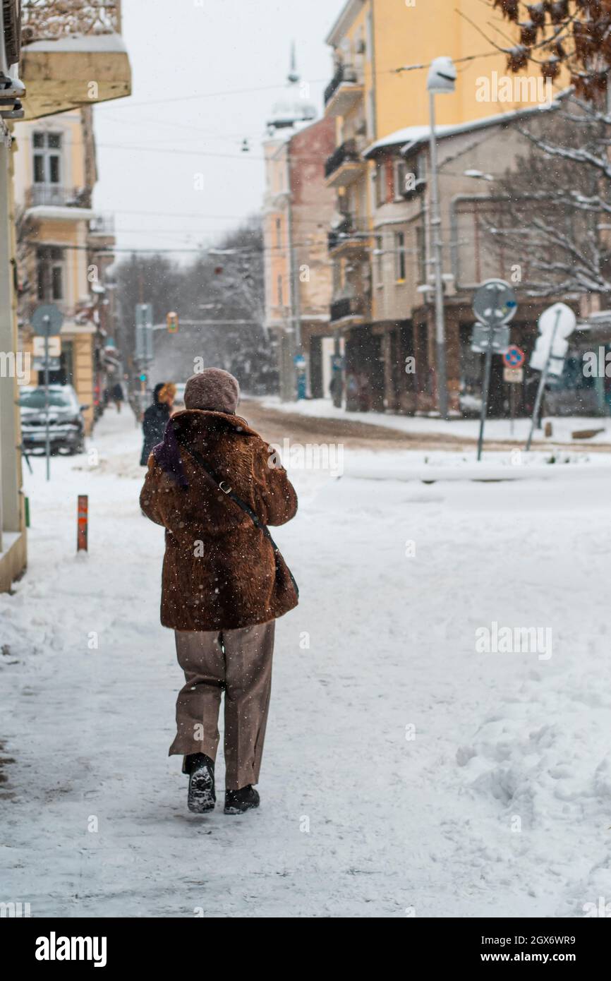 Eine Person läuft im Schnee. Schneesturm in Bulgarien, Europa. Weiß verschneite Straßen der Stadt. Bunte Gebäude in der Ferne Stockfoto