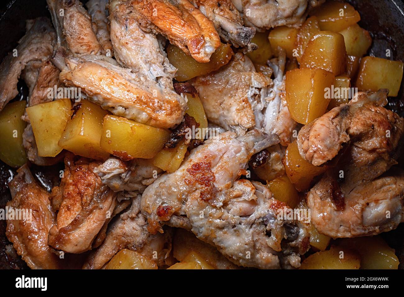 Gebratene Hähnchenflügel mit Kartoffeln werden in einer Pfanne in Nahaufnahme mit geringer Schärfentiefe gekocht Stockfoto