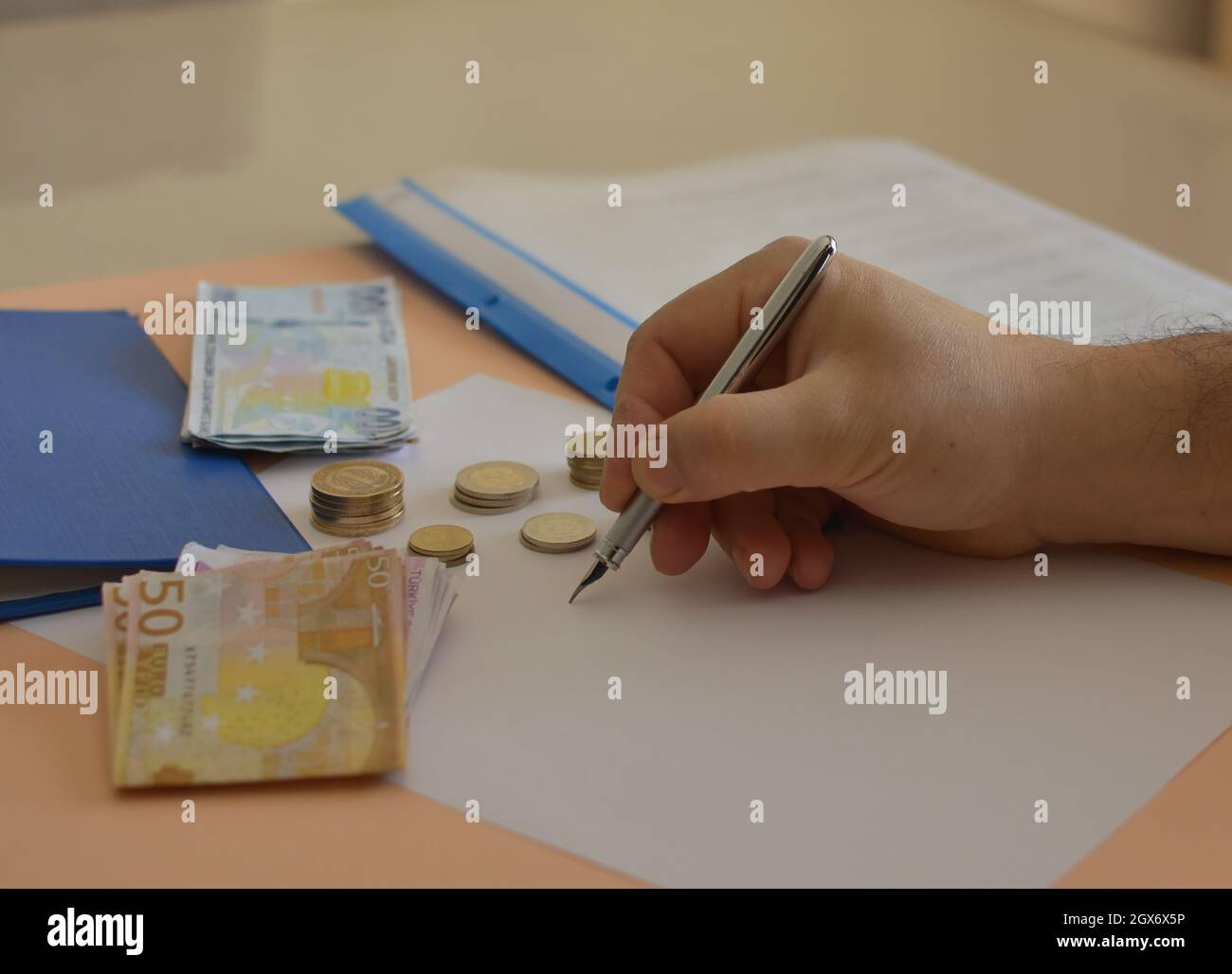Münzen, Akten und eine Hand, die Berechnungen anstellt. Stockfoto