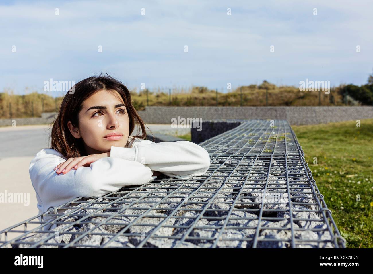 Entspannte junge Frau, die auf einem öffentlichen Park sitzt und wegschaut Stockfoto