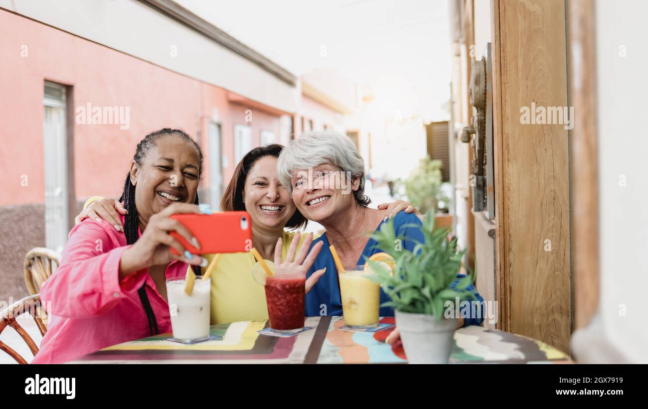 Fröhliche, mehrrassische Freunde, die im Brunch-Restaurant Videogespräche mit dem Mobiltelefon führen - ältere Menschen, die Spaß haben Stockfoto