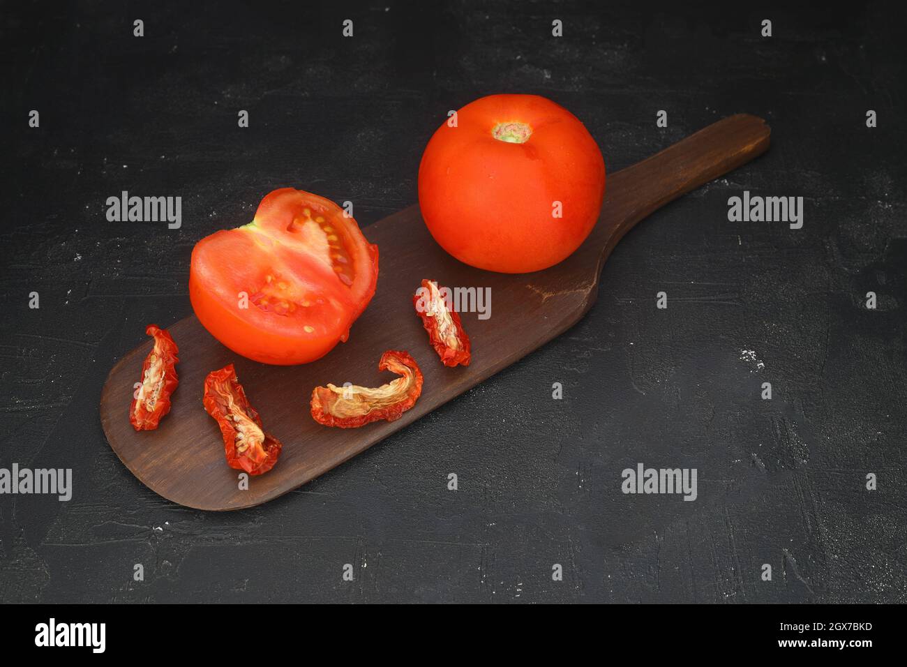 Rote, sonnengetrocknete Tomaten mit Sonnenlicht auf schwarzem Hintergrund. Leckere kleine Scheiben Tomate mit und Olivenöl. Stockfoto