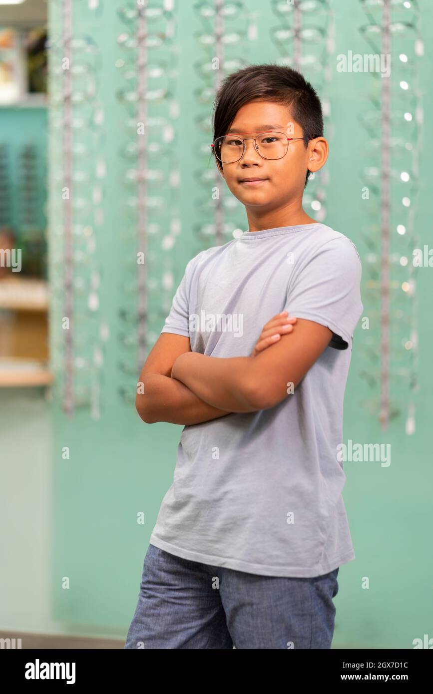 Ein asiatischer Junge, der in einem Optikerladen an einer Brille versucht. Stockfoto