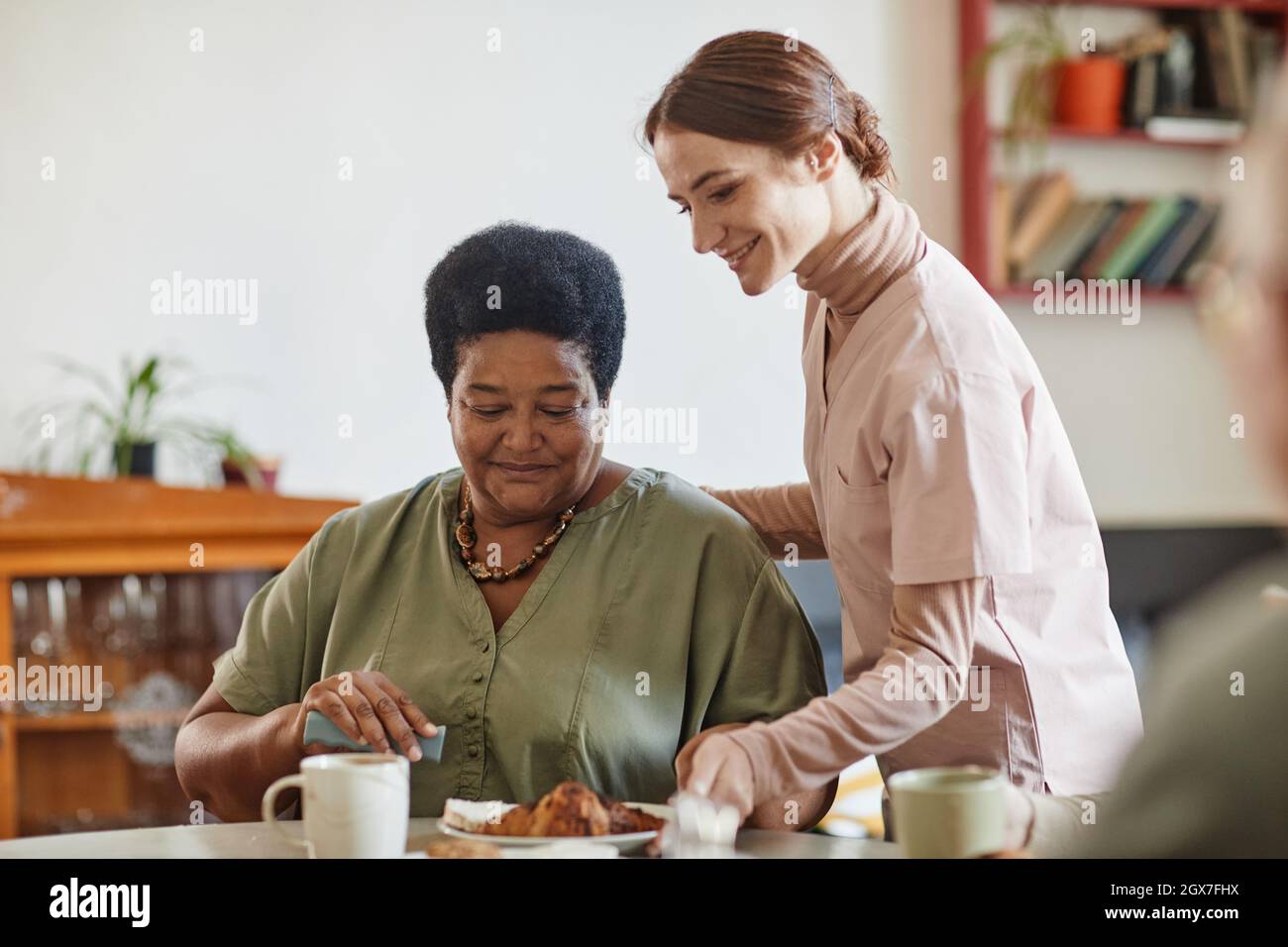 Porträt einer lächelnden jungen Frau, die sich im Pflegeheim um eine ältere afroamerikanische Dame kümmert, Kopierraum Stockfoto