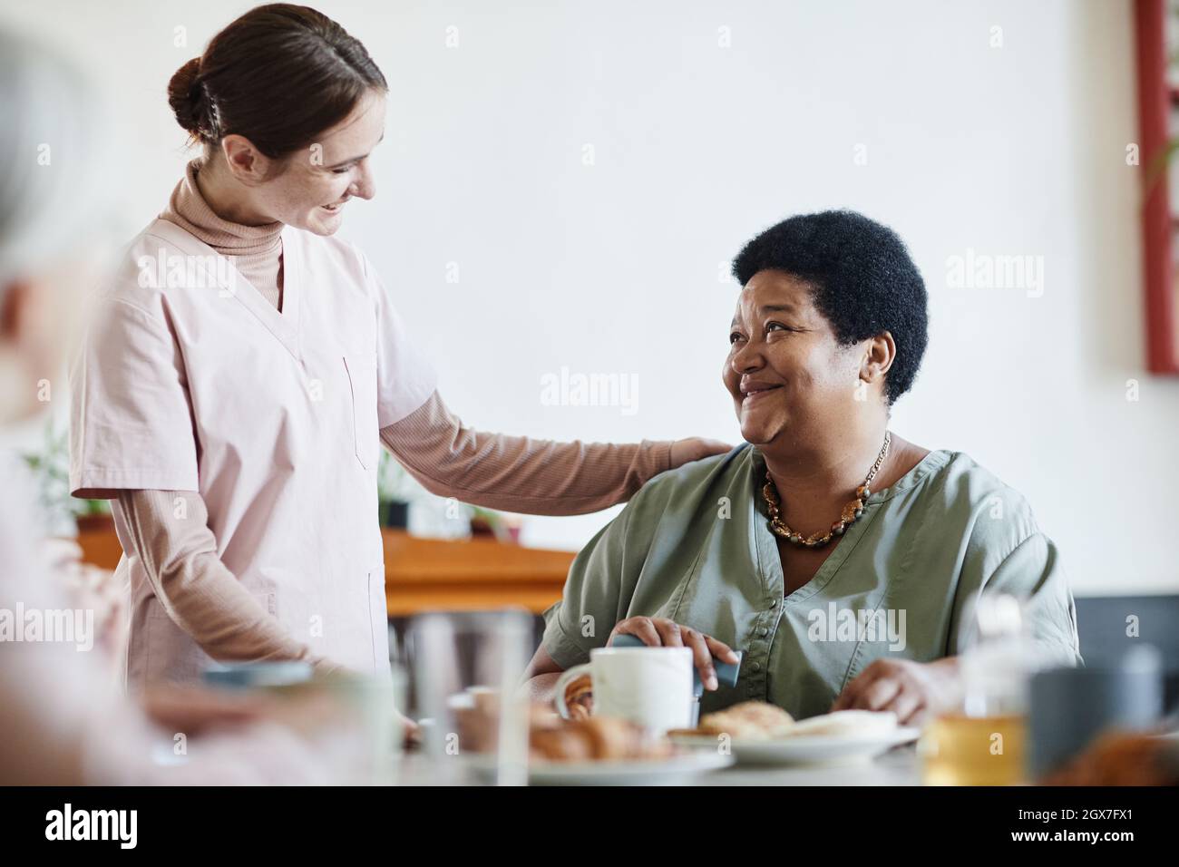 Porträt einer lächelnden jungen Frau, die sich im Pflegeheim um ältere afroamerikanische Patienten kümmert, Kopierraum Stockfoto