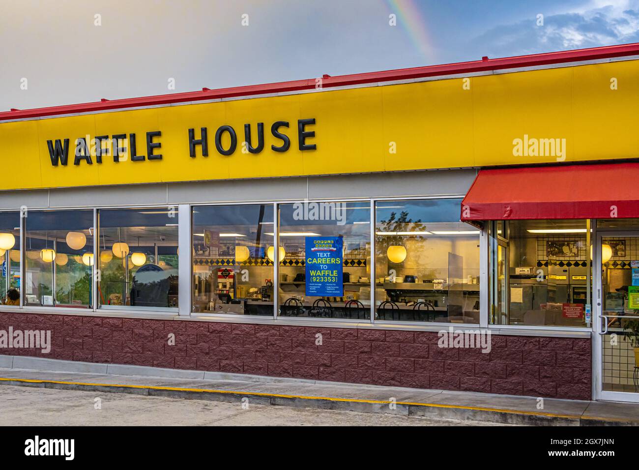 Waffle House Restaurant mit einem ausleihenden Poster im Fenster unter einem hoffnungsvollen Regenbogenhimmel. (USA) Stockfoto