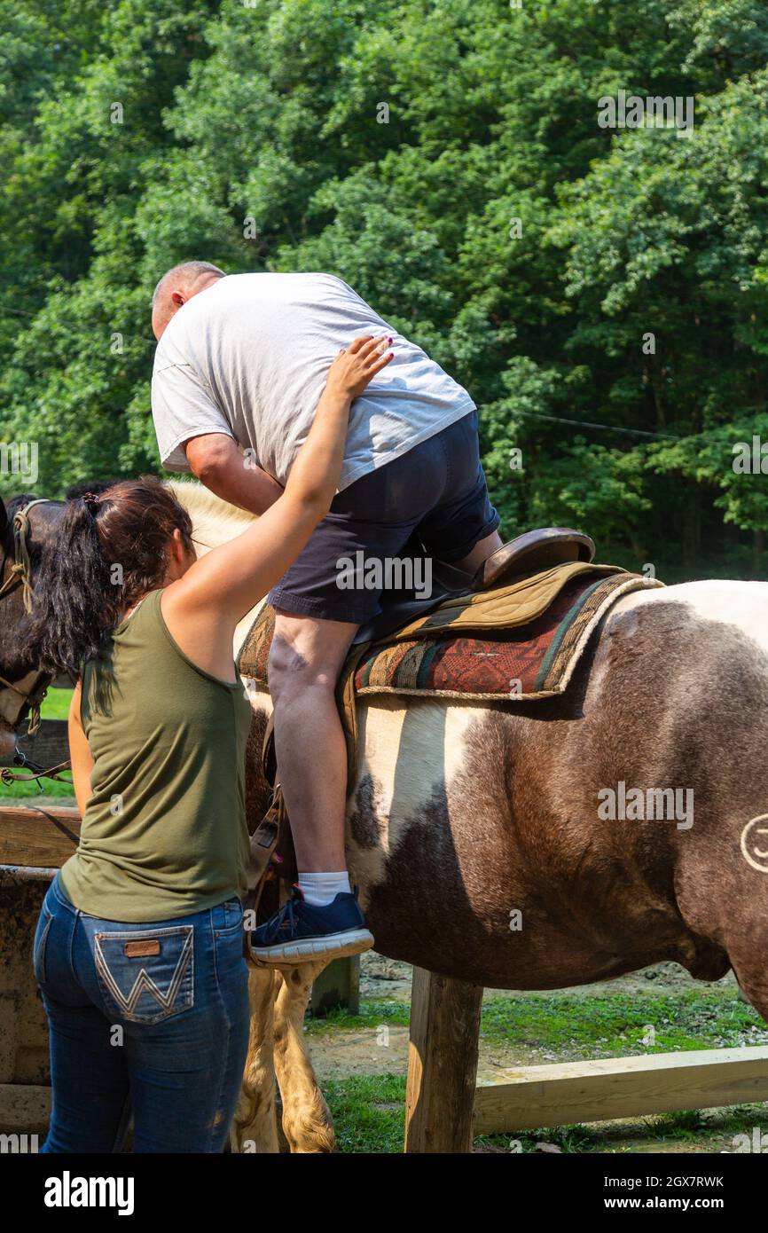 Eine Frau unterstützt einen Mann auf ein Pferd im Brown County State Park in der Nähe von Nashville, Indiana, USA. Stockfoto