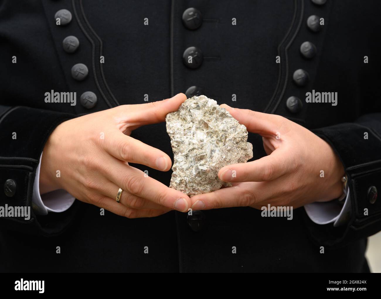 04. Oktober 2021, Sachsen, Altenberg: Ein mit Lithium durchsetztes Stück Erz wird am "Rohstofftag" in den Händen des sächsischen Wirtschaftsministers in einem Bergarbeitergewand vor dem Arno-Lippmann-Schacht gehalten. Im Zinnwald, unter dem Wappen des Erzgebirges an der deutsch-tschechischen Grenze, will die Deutsche Lithium GmbH eine Mine und eine Verarbeitungsanlage bauen. Die Lagerstätte wird auf rund 125,000 Tonnen Lithium geschätzt - und gilt laut der Sächsischen Oberbergbaubehörde als eine der größten Lagerstätten in Europa. Die Deutsche Lithium hat das Projekt i gestartet Stockfoto