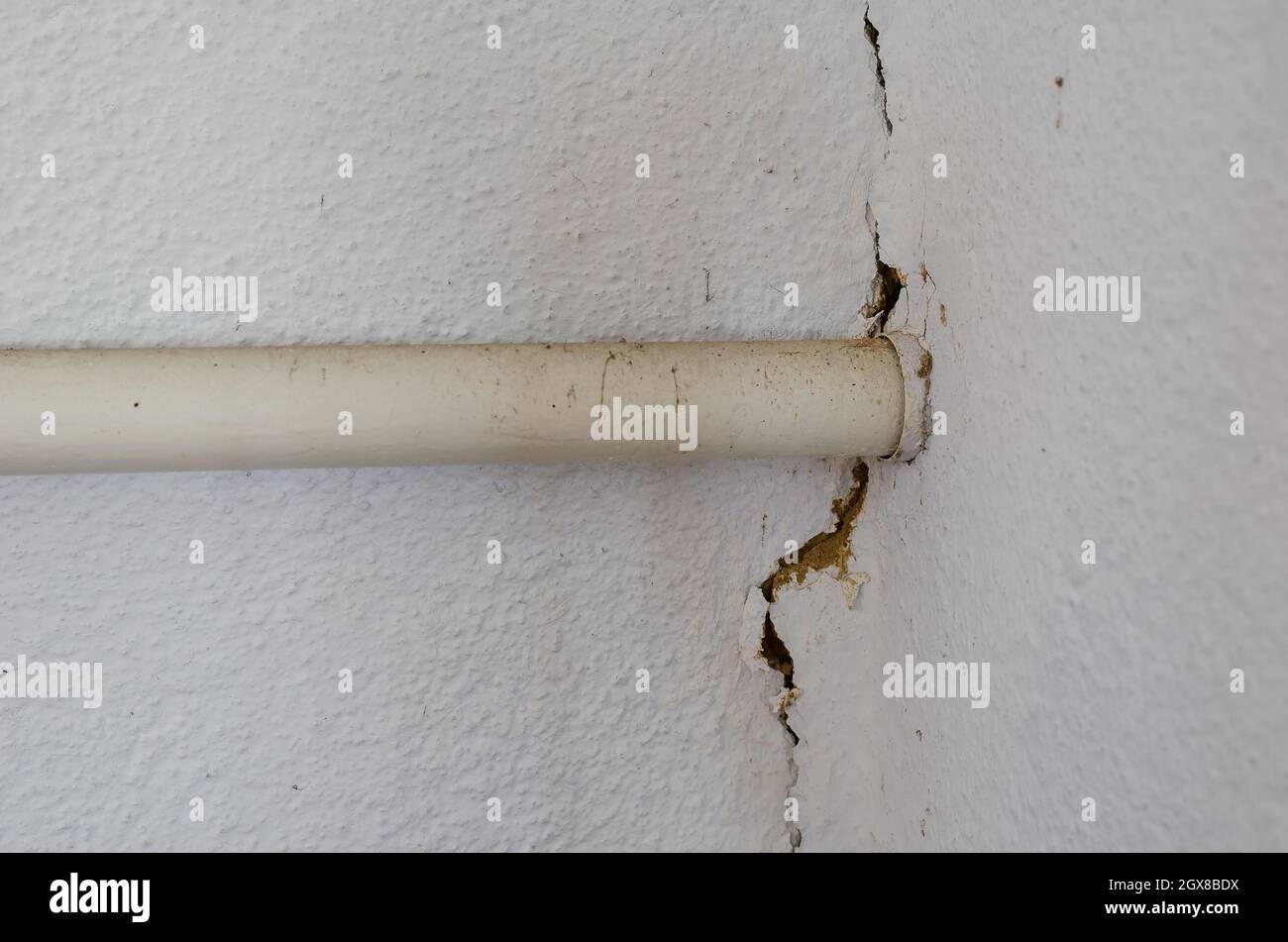 Rissige Wand nach einem Erdbeben. Ein großer langer Riss in der weißen Wand eines Gebäudes. Heizrohr aus weißem Metall. In Innenräumen. Selektiver Fokus. Nahaufnahme. Stockfoto