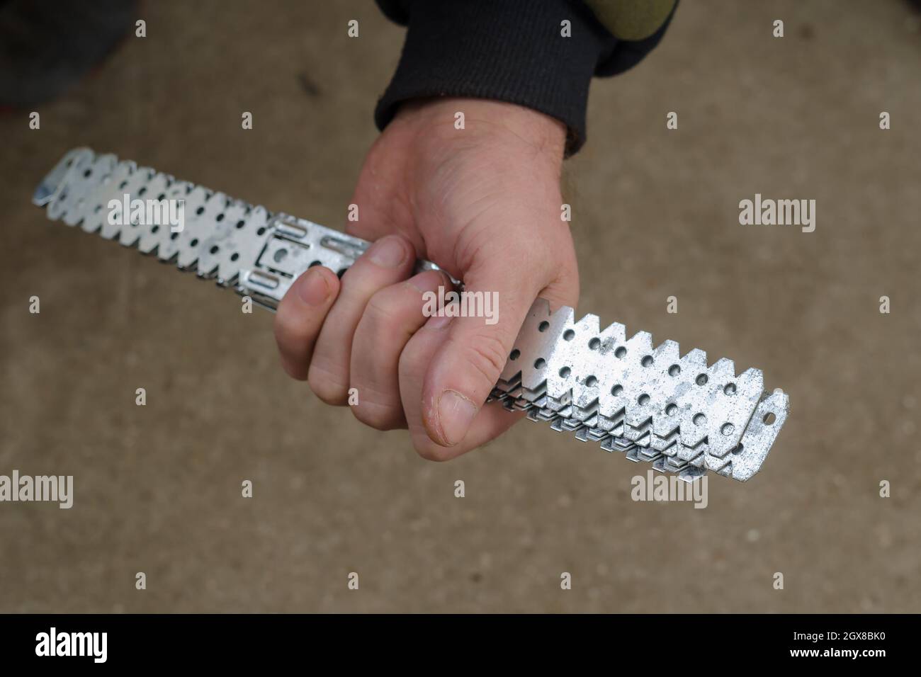Man hält lange perforierte verzinkte Stahlplatten. Befestigung für den Bau von Gipskartonrahmen. Trockenbauhalterungen. Selektiver Fokus. Stockfoto