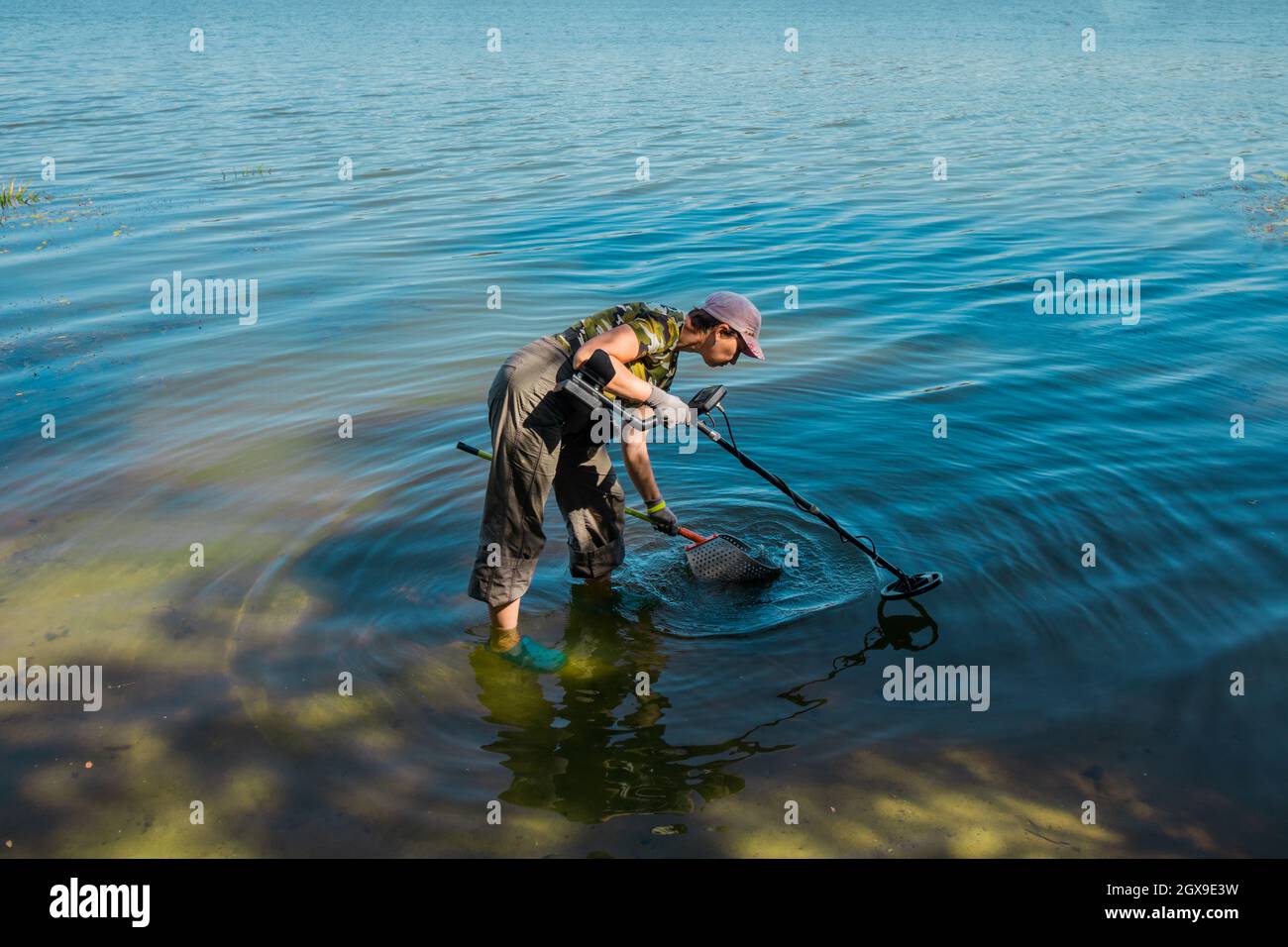 Eine Frau sammelt an einem sonnigen Tag mit einem Metalldetektor Metall im Fluss. Stockfoto